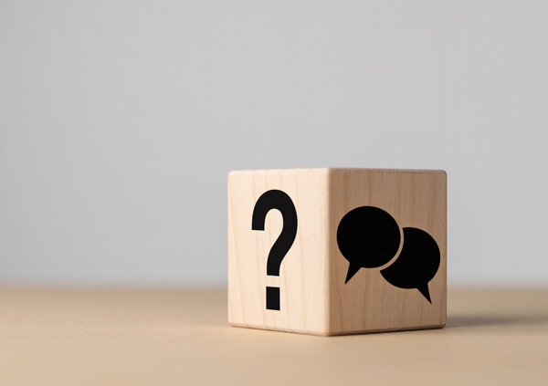 Wooden blocks featuring a question mark and a speech bubble symbol on a table. The illustration represents frequently asked questions, information sharing, customer support, and access to helpful guidance.