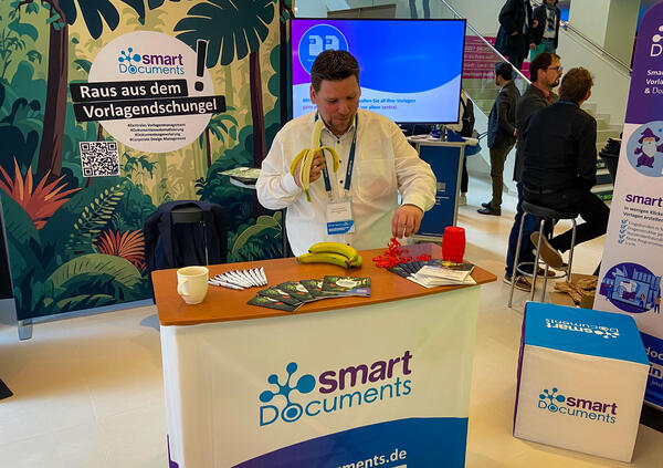 Foto von Christoph Winkelmann der am SmartDocuments Stand eine Banane isst und für die Olympische Disziplin "Affenfassen" übt.