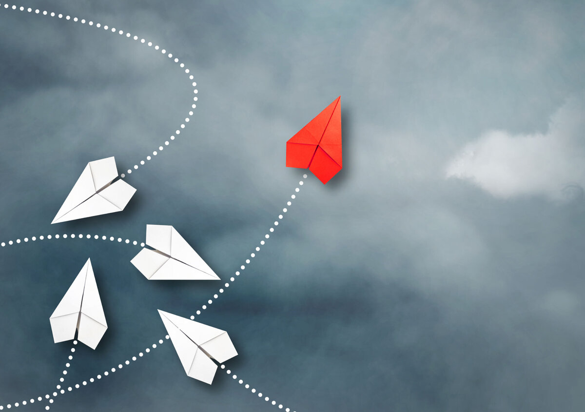 Red paper airplane flying ahead of several white paper airplanes, symbolizing customer success, innovation, and leadership.
