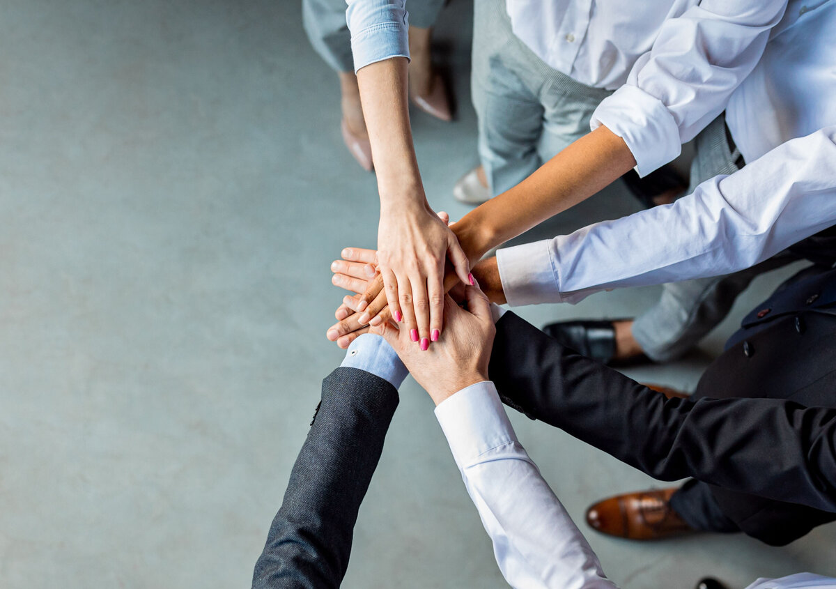 Multiple employees placing their hands on top of each other, symbolizing teamwork, collaboration, trust, and shared success in a professional environment.