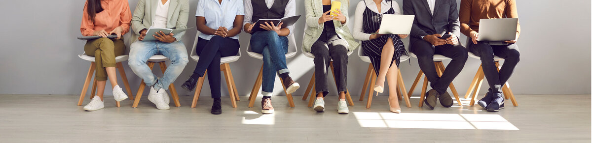 Multiple candidates sitting in a row with laptops, tablets, and smartphones, waiting for a job interview, symbolizing career opportunities, recruitment, and professional growth.