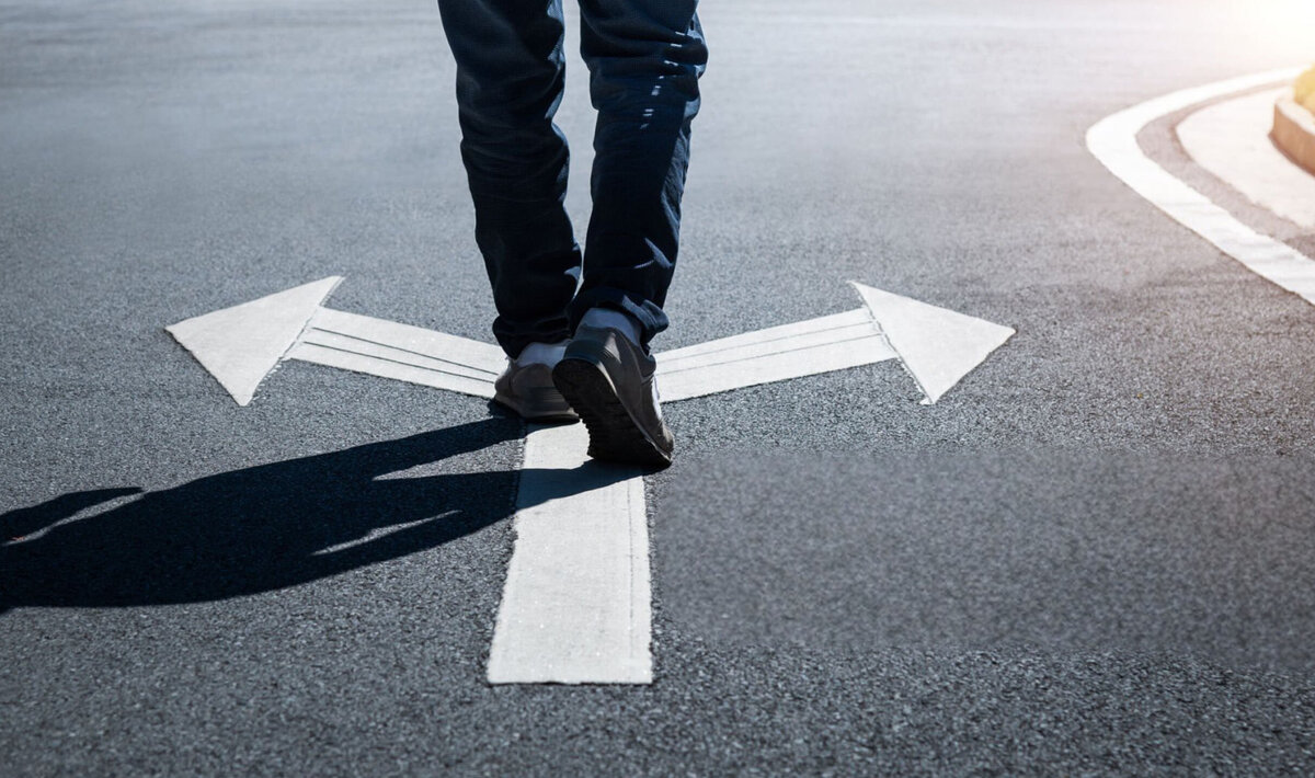 Person standing at a fork in the road. Directional markers with arrows pointing left and right highlight the choice between two possible paths or options. The illustration symbolizes decision-making, flexibility, and selecting the solution that best fits individual requirements.