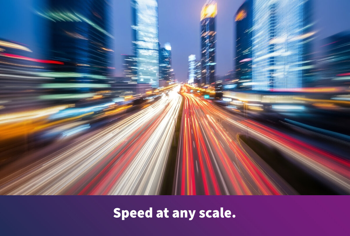 Nighttime view of a modern metropolis with skyscrapers and a multi-lane roadway. The light trails of passing vehicles convey a sense of high speed. Along the bottom edge of the image, the text reads: &laquo;Fast at any scale.