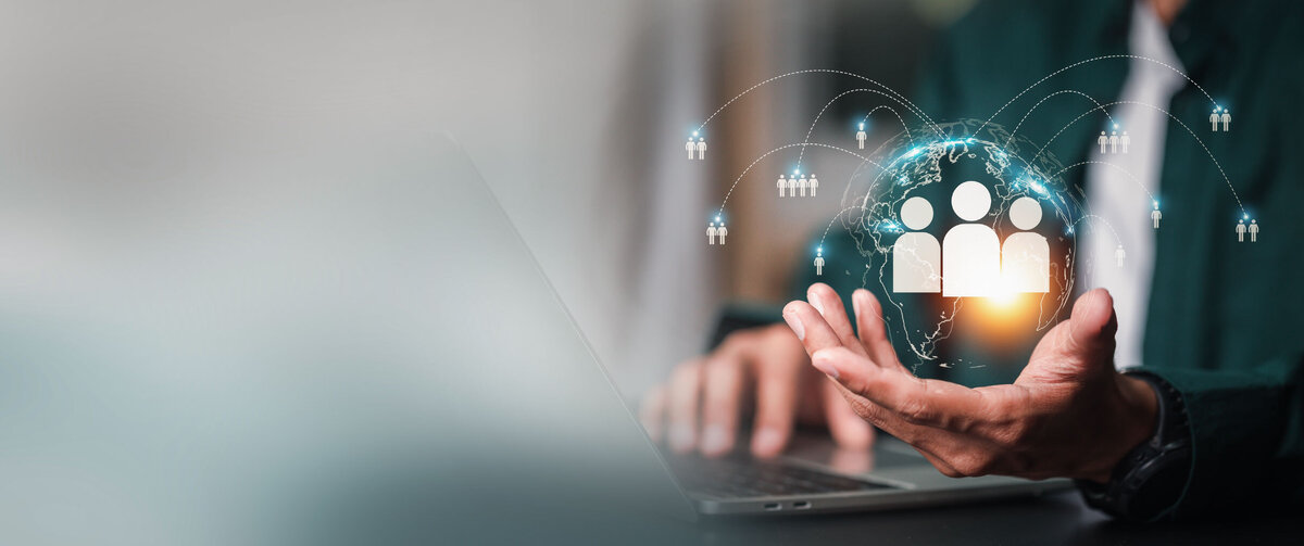 Person som arbetar p&aring; en b&auml;rbar dator samtidigt som hen h&aring;ller en digital jordglob med sammankopplade personikoner, vilket symboliserar digital rekrytering, HR-tj&auml;nster, talent management och global uppkoppling mellan medarbetare.
