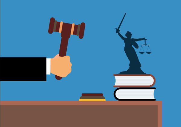 Vektorgrafik: Richtertisch auf dem sich Gesetzesbücher und die Justizia befinden. Von der linken Seite kommt ein Arm mit Richterhammer ins Bild.