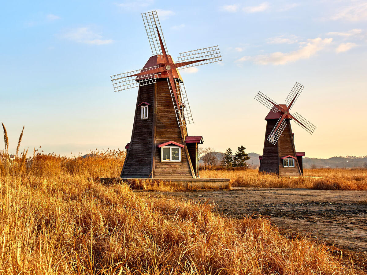 Bild vergrößern: Fotoaufnahme zweier Windmühlen bei Sonnenschein.