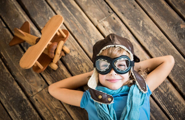 Foto: Kind mit Fliegerbrille und Fliegermütze, daneben ein Holzflugzeug.