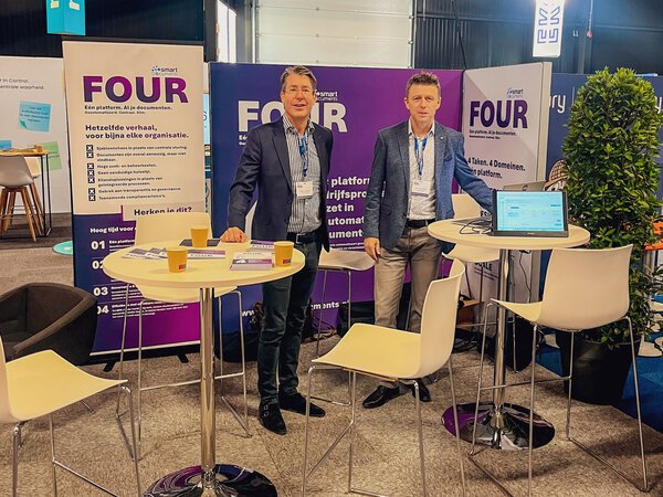SmartDocuments presenteert het documentplatform FOUR op CorporatiePlein 2026. Twee medewerkers staan voor banners en een softwaredemo op de beursstand.